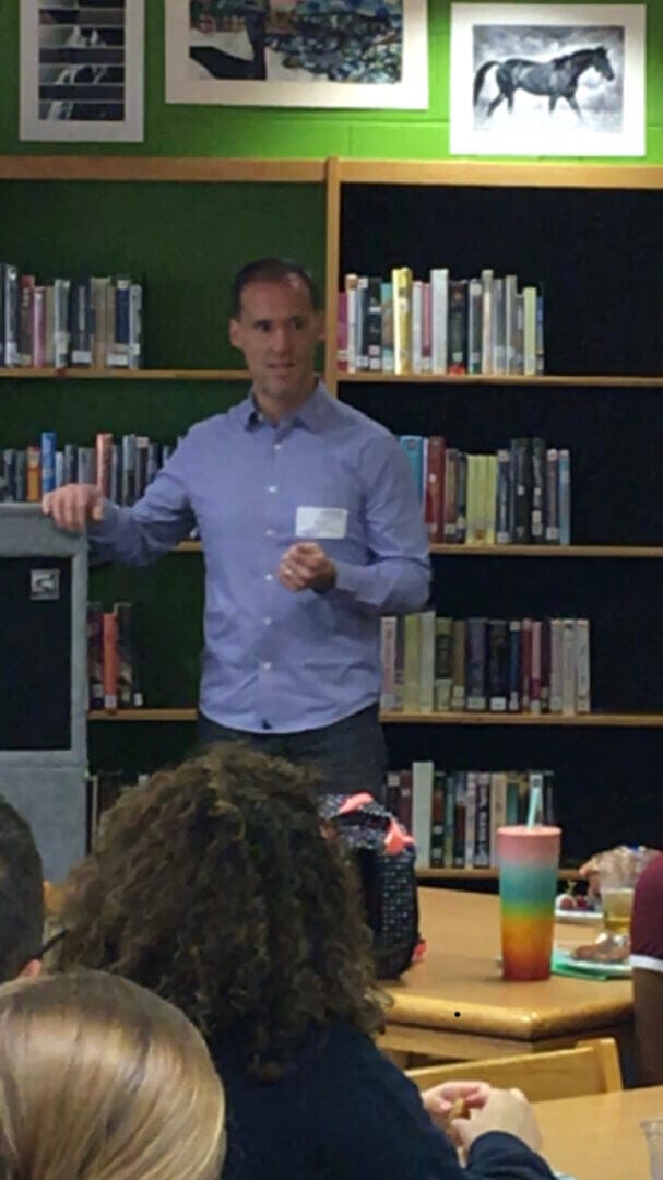 Speaker engaging audience in a library setting, enhancing teamwork skills, only available at Elevate Your Organization's Culture and Performance With CEEK.