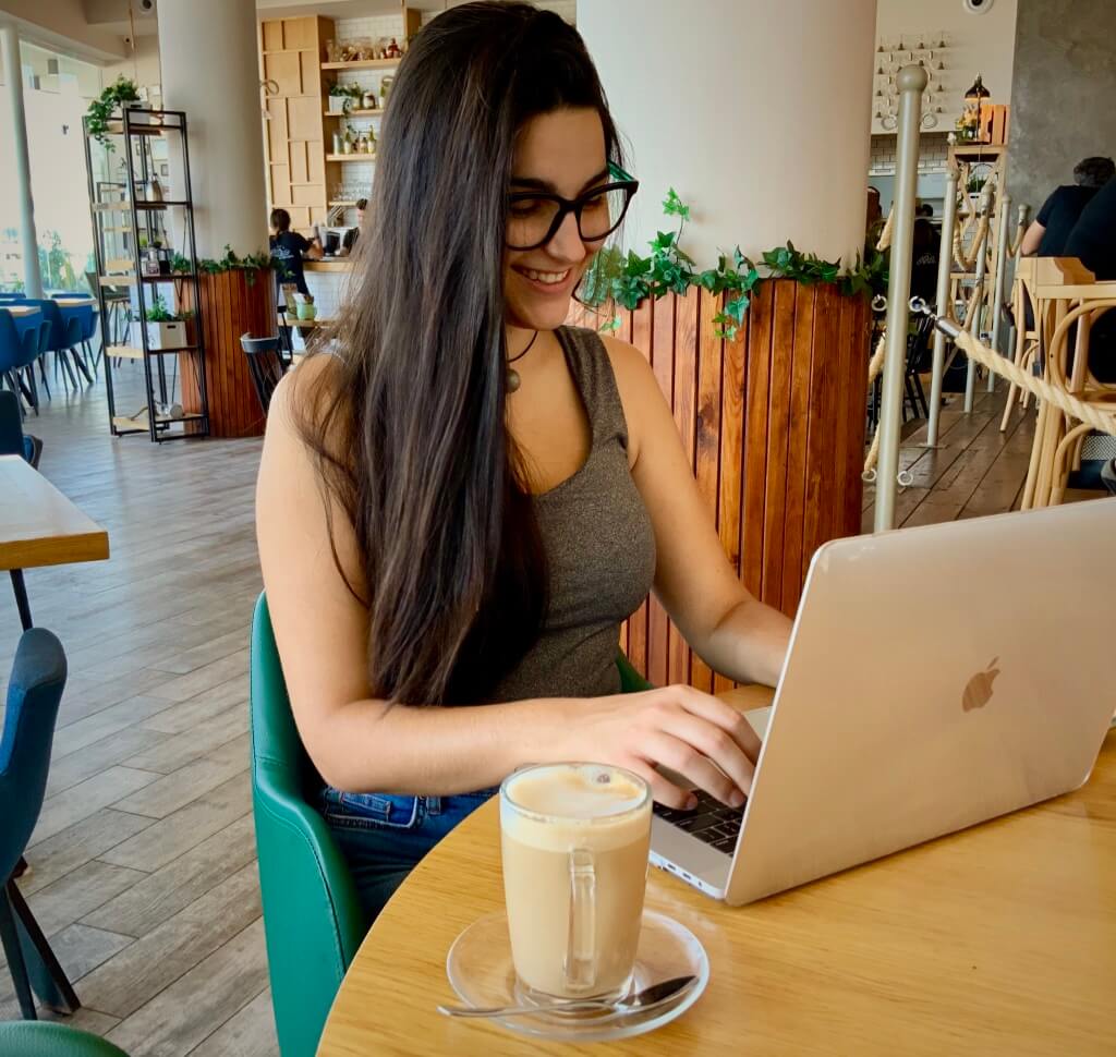 Smiling woman working on a laptop in a cozy cafe, enhancing productivity with Elevate Your Organization's Culture and Performance With CEEK.