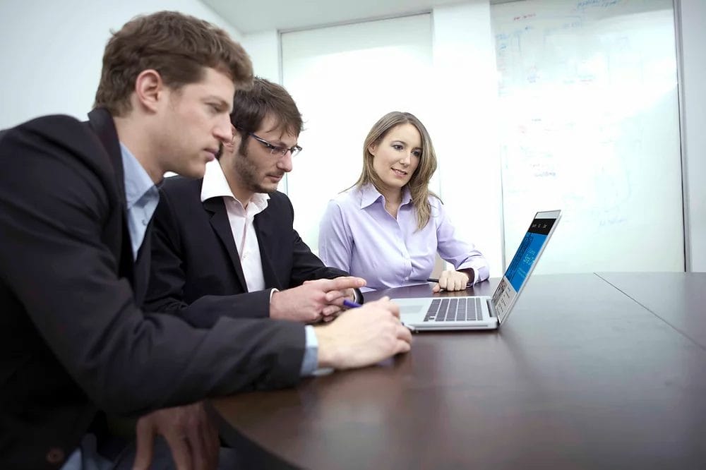 Team collaboration around a laptop in an office setting, showcasing Elevate Your Organization's Culture and Performance With CEEK expertise.