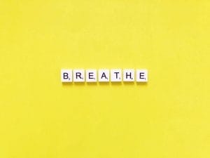 Scrabble tiles spell out "breathe" on a yellow background