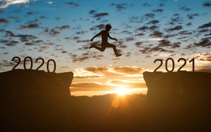 Happy new year 2021 concept. Silhouette of man jump on the cliff between 2020 to 2021 years over sunset or sunrise background.